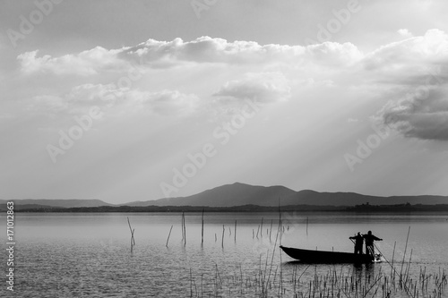 Two fishermen on a little boat with a fishing net and distant sun rays in the background