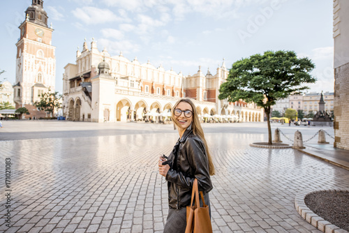 Portrait of a young happy woman tourist in front of the cloth hall on the Market square during the morning light in Krakow, Poland