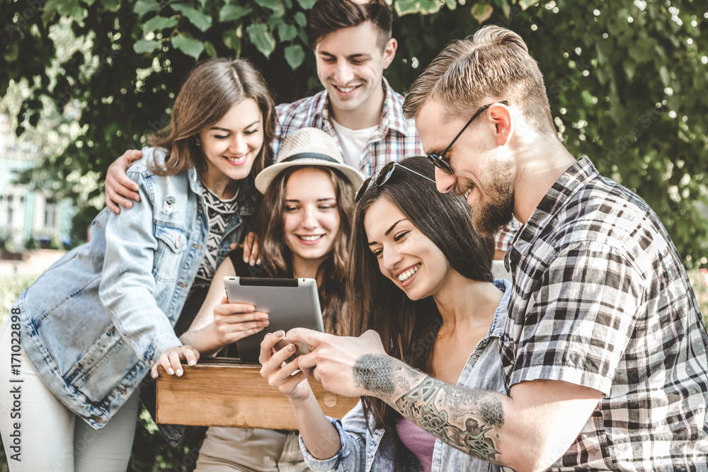 Obraz premium Having the best time with friends.College students using laptop while sitting at wooden table in campus.