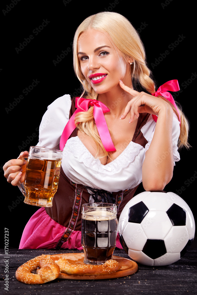 Young sexy Oktoberfest girl - waitress, wearing a traditional Bavarian dress, serving big beer mugs and taking soccer ball on black background. Young sexy Oktoberfest girl - waitress, wearing a traditional Bavarian dress, serving big beer mugs and taking soccer ball on black background.