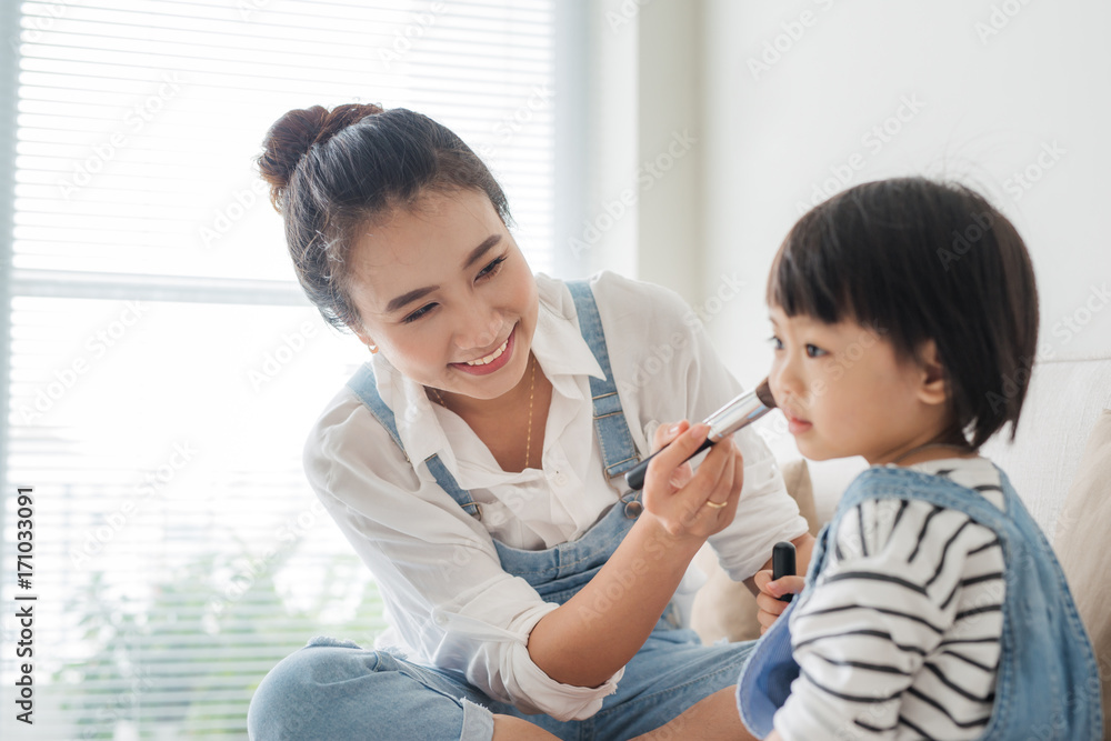 Cute little girl and her beautiful mother are doing makeup while sitting on couch at home Cute little girl and her beautiful mother are doing makeup while sitting on couch at home