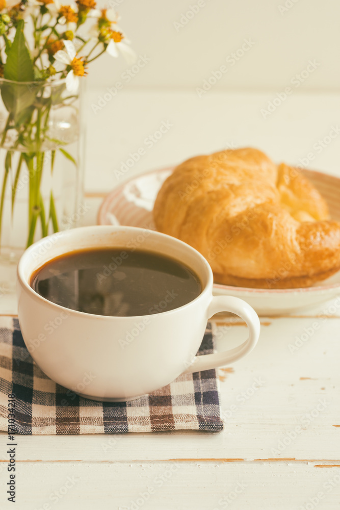 Black coffee or americano served with homemade croissant on plate. Delicious and quick breakfast with fresh croissant and coffee. Croissant and black coffee for breakfast on wood table in vertical. Black coffee or americano served with homemade croissant on plate. Delicious and quick breakfast with fresh croissant and coffee. Croissant and black coffee for breakfast on wood table in vertical.