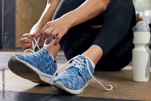 Closeup of unrecognizable young woman fixing her shoes taking break during workout in modern gym