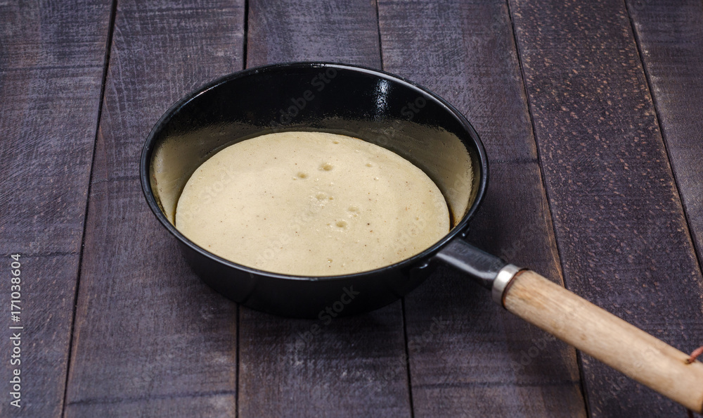 Raw pancake in a frying pan on a dark background