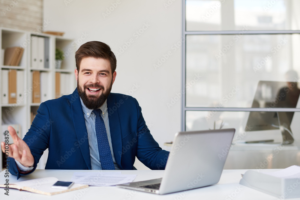 Portrait of successful bearded businessman smiling happily while working at desk i9n modern office
