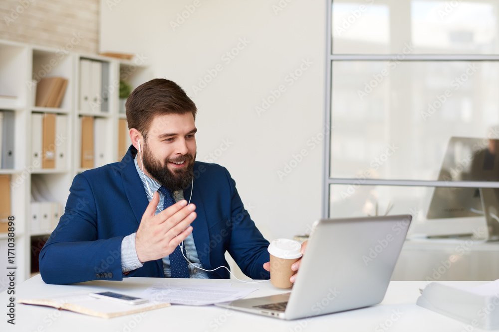Portrait of smiling bearded businessman speaking with partner via laptop by video chat meeting