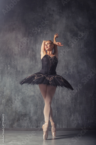 Young beautiful woman prima theater in a black festive pack, white pantyhose, white pointe shoes beautifully dancing russian ballet in a black dance studio photo