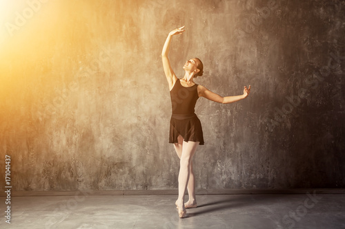 Young beautiful woman prima theater in a black pack, white pantyhose, white pointe shoes beautifully dances Russian ballet in a black dance studio...