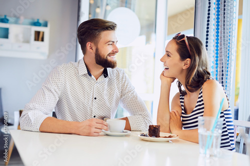 Young attractive couple talking and laughing in cafe. looking at each other while having coffee and cake in cafeteria