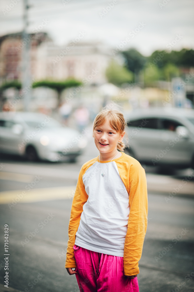Outdoor portrait of pretty little teenage girl in a city, wearing yellow and white long sleeve baseball t-shirt and bright pink trousers