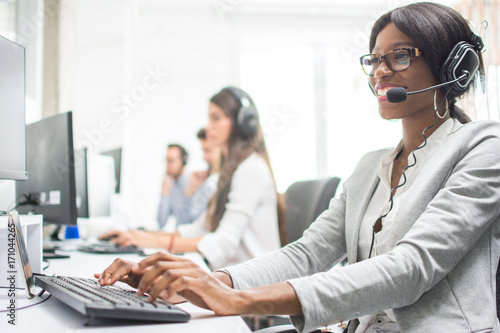 Friendly female helpline operator with headphones in office. Agent customer service representative: business and office concept.