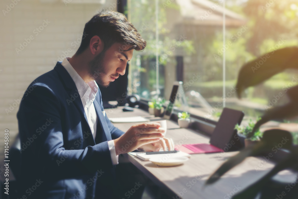 Young businessman wearing suit and using laptop indoor in cafe. Business concept. Drinking coffee during break.