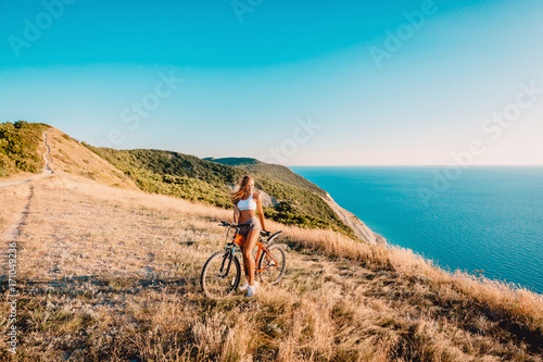 Beautiful woman on red mountain bicycle in the mountains and background of sea