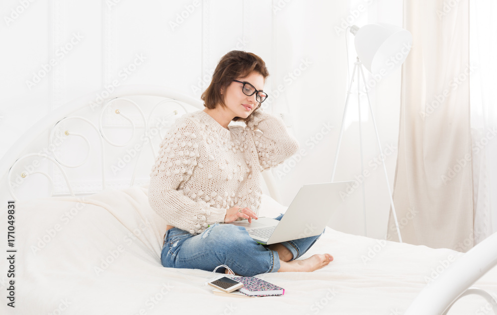 Young woman freelancer with laptop in bed
