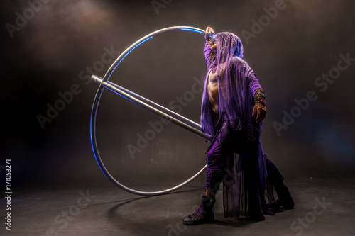 Fairy-tale character assassin in a purple cloak with a hood with two large cyr wheel hoops