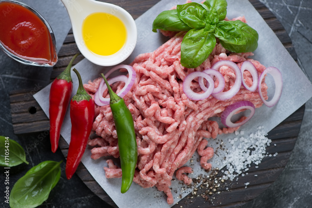 Closeup of raw fresh pork minced meat with chili peppers, olive oil, onion, green basil, sea salt and spices, view from above Closeup of raw fresh pork minced meat with chili peppers, olive oil, onion, green basil, sea salt and spices, view from above