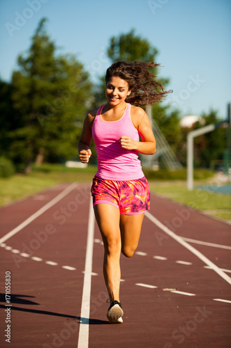 active young woman runs on atheltic track on summer afternoon