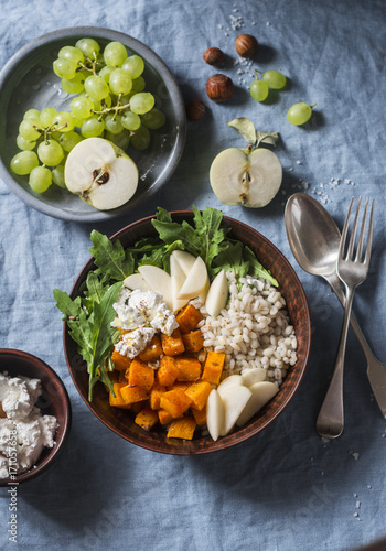 Full bowl with baked sweet potatoes, barley, arugula and apples. Vegetarian buddha bowl with autumn vegetables and grains, on a blue background, top view