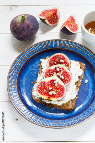 Figs and cheese on a bread. Sandwich on a plate, white wooden background.