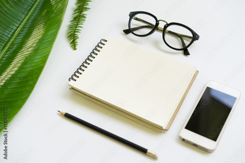 Creative Flat lay design of blank notebook, smartphone,glasses and pincil with green leaf on white background. Creative Flat lay design of blank notebook, smartphone,glasses and pincil with green leaf on white background.