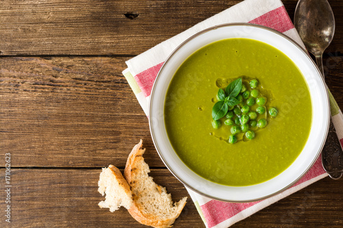 Green pea soup in bowl on wooden table photo