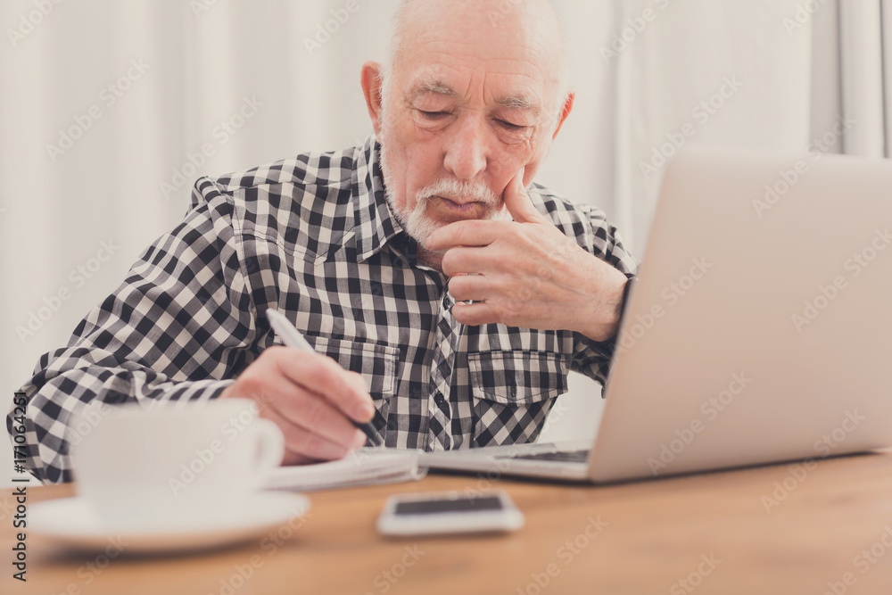 Mature man using laptop and writing in notepad Mature man using laptop and writing in notepad