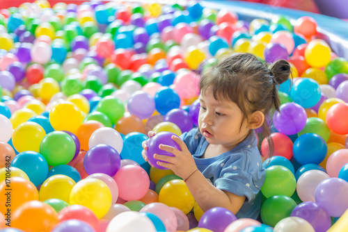 Cute Asian baby girl holding purple ball in colorful plastic ball pool