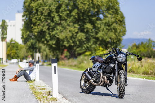 Motorcycle rider sitting near custom made scrambler style cafe racer photo