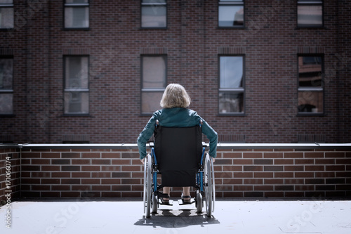 lonely woman on wheelchair surrounded by bricked buildings