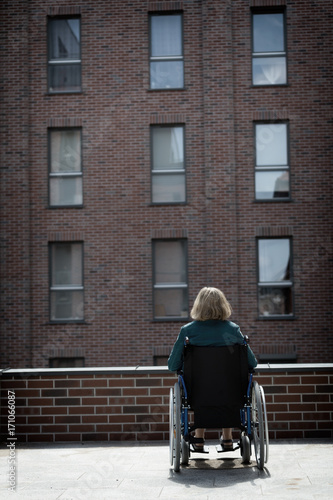 lonely woman on wheelchair surrounded by bricked buildings © Adam Wasilewski