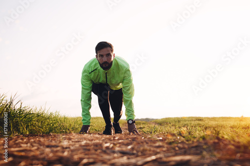 Male athlete at sportswear in running start pose on outdoor field. Bright sunset