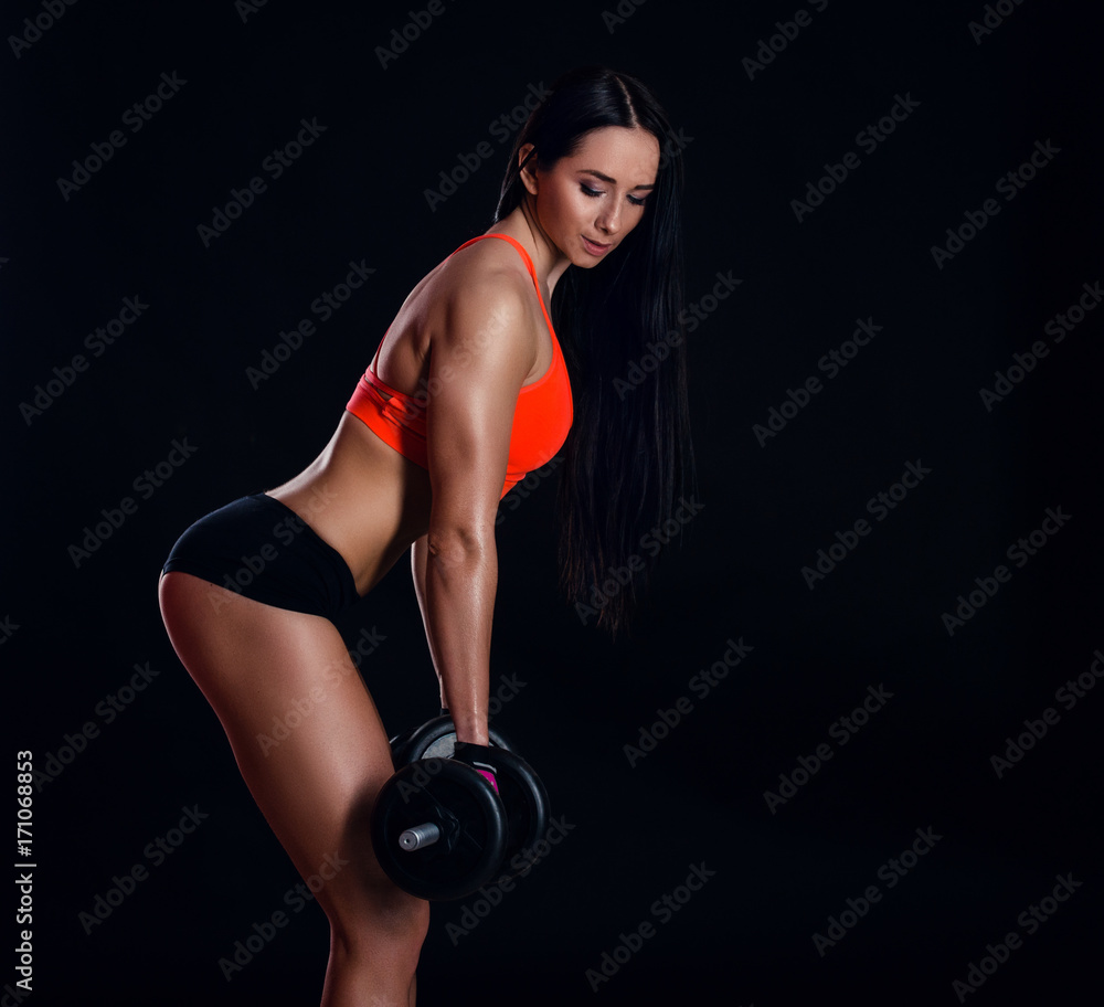 Fototapeta premium Nice sexy girl doing workout with dumbbells isolated over black background. Athletic young woman do a fitness workout with weights.