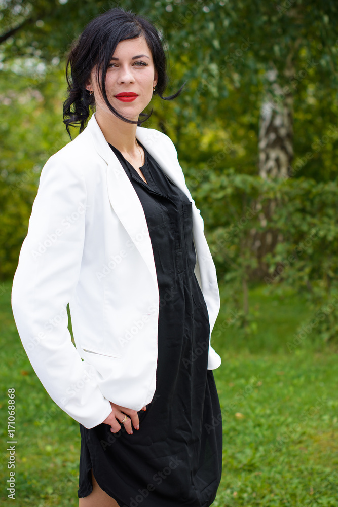 Business woman near the office, a stylishly dressed brunette in a black dress and a white jacket. A lady is waiting for her colleagues near the office Business woman near the office, a stylishly dressed brunette in a black dress and a white jacket. A lady is waiting for her colleagues near the office
