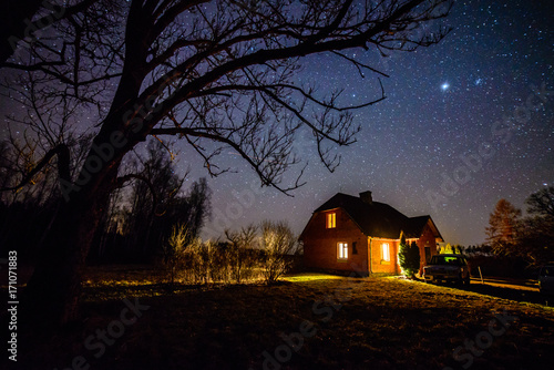 The Milky Way in night sky with stars over wooden country house at night