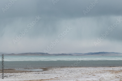 panoramic view of watery surface of lake with snow on coast and storm clouds in sky