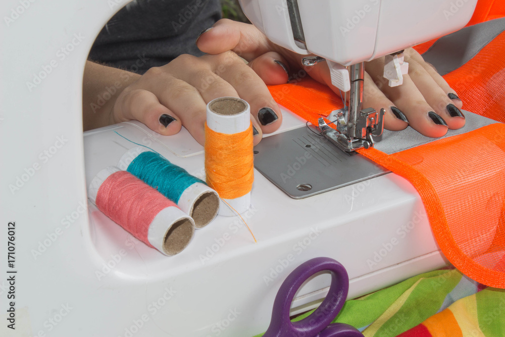 woman's hands using sewing machine with reels of colour threads woman's hands using sewing machine with reels of colour threads