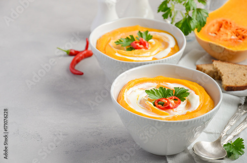 Pumpkin soup with cream and parsley on a grey concrete or stone background, selective focus, copy space