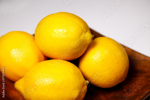 Four ripe fresh lemons on a wooden plate on a white background
