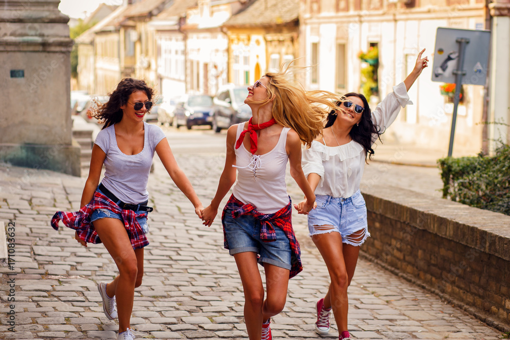 Three young female friends walking in city street laughing and having fun.