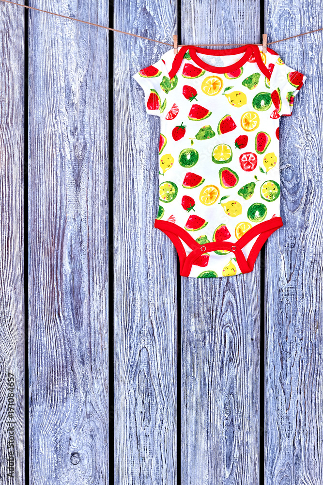 Obraz premium Baby soft bodysuit hanging on clothesline. Rope with drying newborn girl romper on wooden background, copy space.