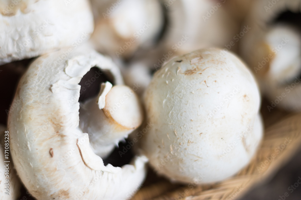 Close-up: white mushrooms of champignon lie on a wicker plate on a table. They are good to eat and ready for cooking. Concept: healthy vegetarian food. Close-up: white mushrooms of champignon lie on a wicker plate on a table. They are good to eat and ready for cooking. Concept: healthy vegetarian food.