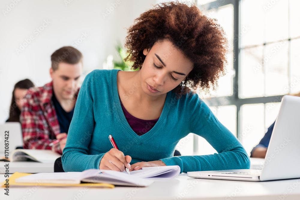 Young female student with a serious facial expression concentrating while writing an essay, during class in an international university Young female student with a serious facial expression concentrating while writing an essay, during class in an international university