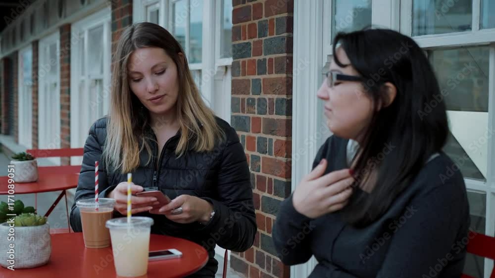 Two young women sit in a street cafe and relax Two young women sit in a street cafe and relax