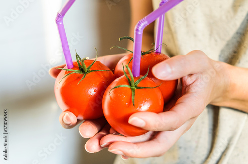 Three Ripe Red Tomatoes with Straws in Woman Hands on Bright Background. Fresh Juice Healthy Food Concept. Tomato as a Vessel with Fresh Juice photo