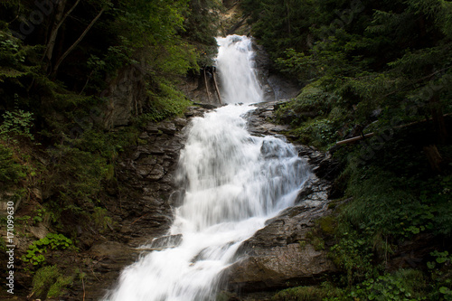 Mountain waterfall in a forest in Valle d'Aosta, flows between trees and rocks.