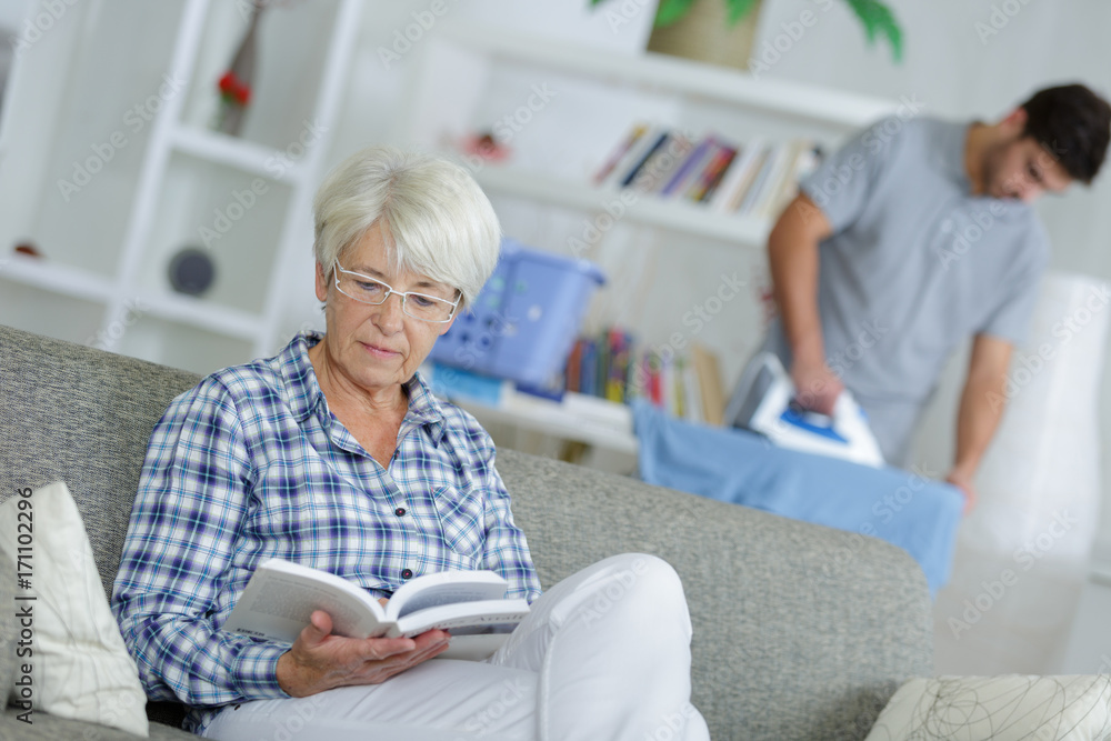 home help man ironing and senior lady reading a book home help man ironing and senior lady reading a book