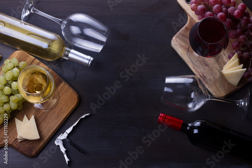 Bottles of red and white wine with wine glasses and grape on table with copy space