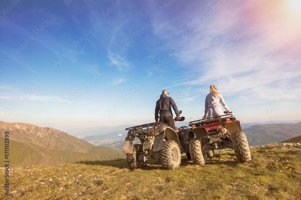 Obraz premium Rear view of young pair near atv. Man is showing something in distance to her girlfriend.