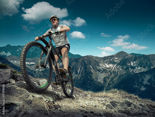 Man in helmet and glasses stay on the bicycle under sky with clo