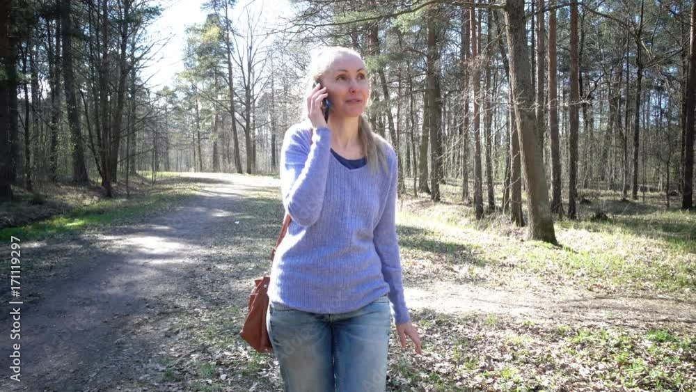 Slow motion,The young happy woman in a blue jacket and jeans lit with kontrovy light goes on a path of the park and speaks by phone Slow motion,The young happy woman in a blue jacket and jeans lit with kontrovy light goes on a path of the park and speaks by phone